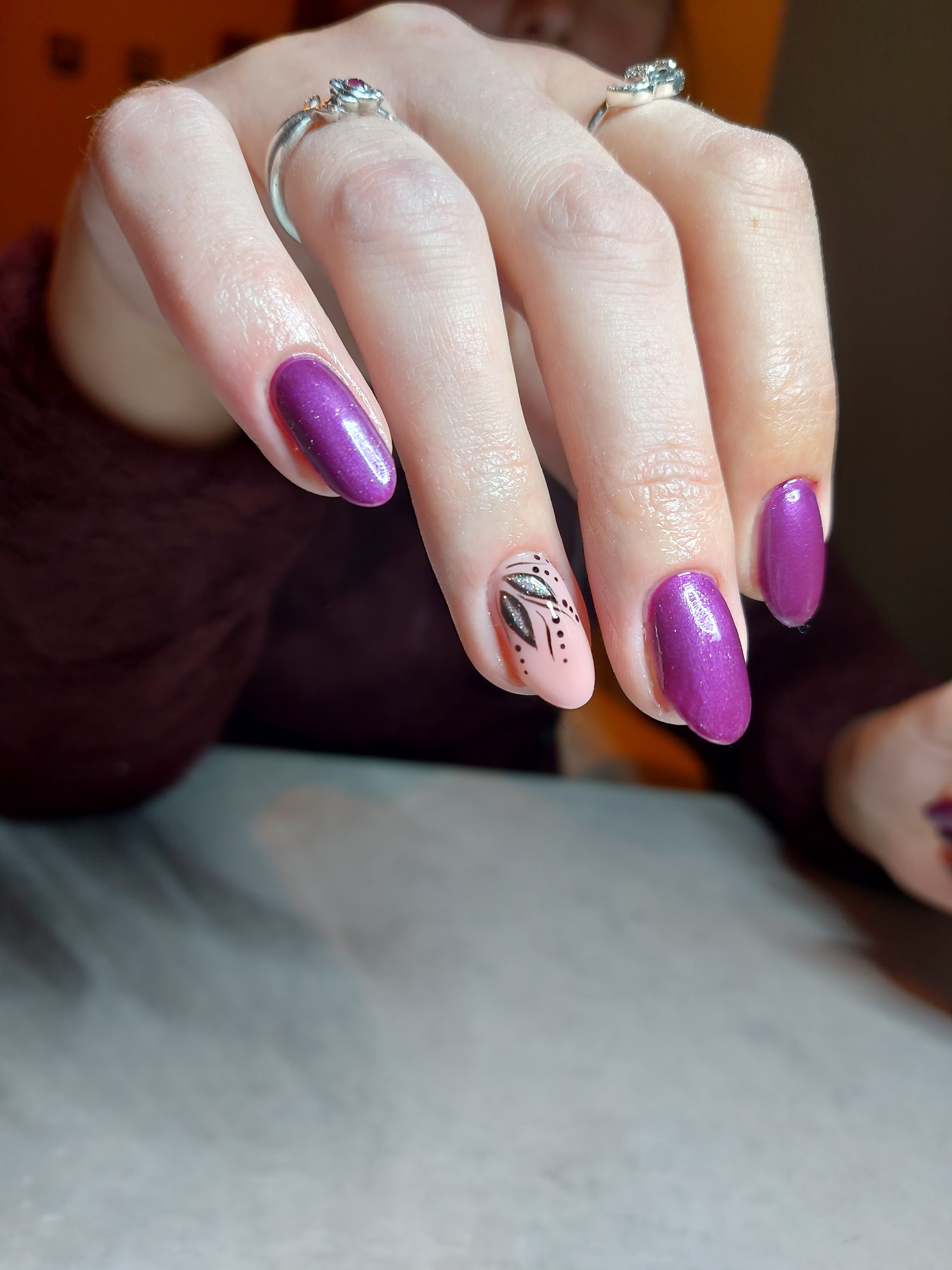 Paarse glitternagels met een accentnagel met zwarte bladlijnen